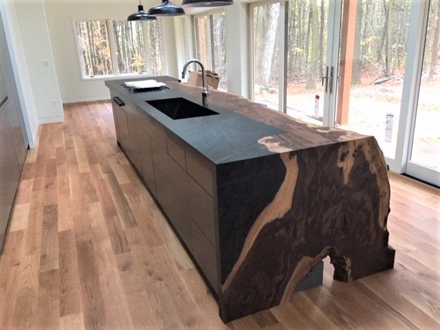 a large kitchen island made out of wood with two sinks in the center and windows to the outside