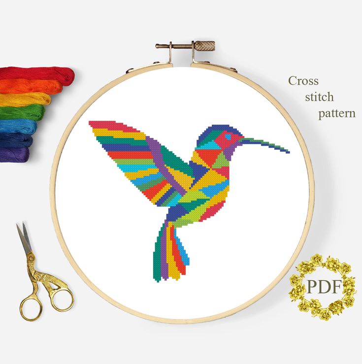 a cross stitch hummingbird pattern with scissors, thread and spools next to it