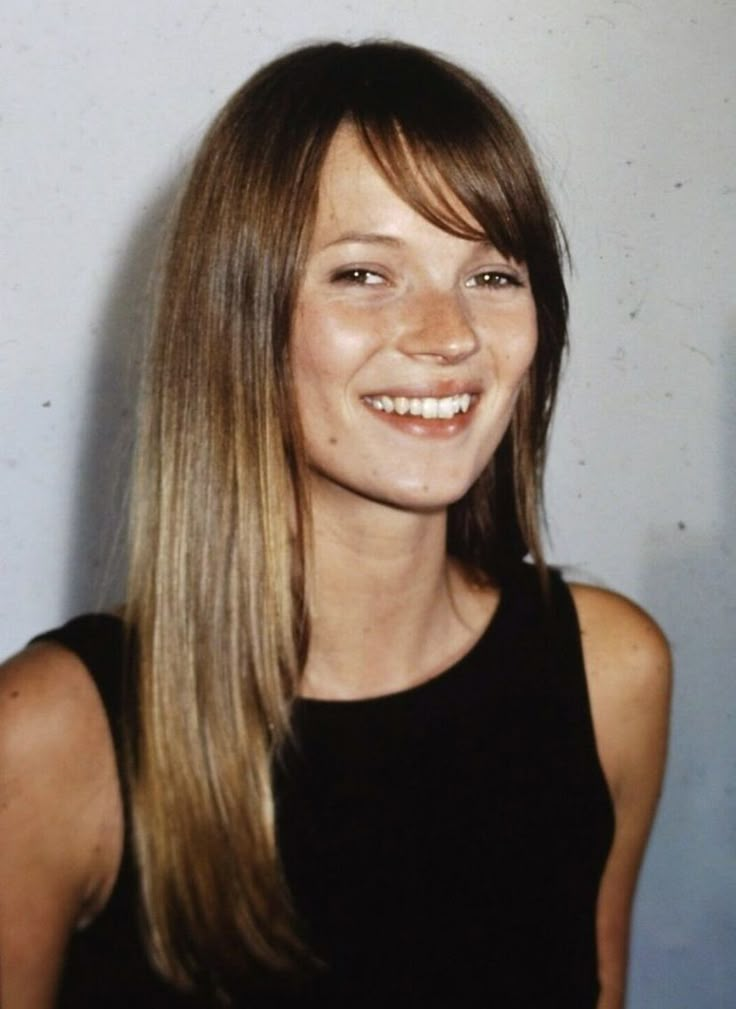 a woman with long hair smiling at the camera and wearing a black tank top in front of a white wall