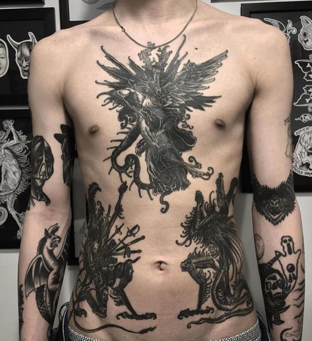 a man with many tattoos on his body and chest is standing in front of a wall