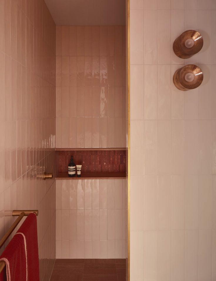 a pink tiled bathroom with gold fixtures and red towel racks on the wall next to it