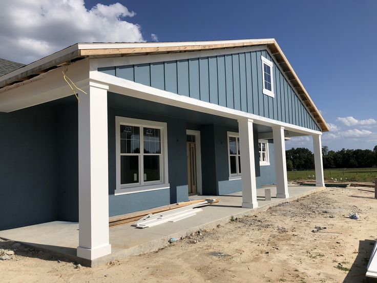 a blue house with white trim on the front and side walls is under construction in an open field