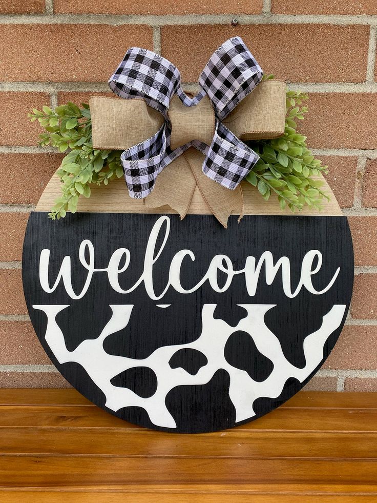 a welcome sign with a bow hanging on it's side, in front of a brick wall