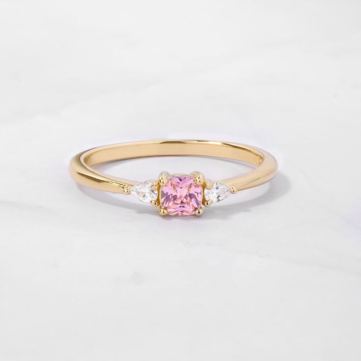 Sweet, simple, and dainty ring. Perfect for a minimalist look, or for stacking. It adds a fun pop of color to your look! Featuring a pink cushion cut stone with pear stones adorning both sides - making this a delicate and beautiful ring!Pink Stones are said to indicate a feeling of rest and peacefulness. It also said that that a person wearing the ring will feel loving, affectionate and happy. Made of 925 Sterling Silver Available in 14k Gold or Rhodium Plating We use a THICK 14k Gold plating - Pink Cushion Cut Diamond Ring Gift, Pink Cushion Cut Cubic Zirconia Rings, Pink Cubic Zirconia Crystal Promise Ring, Minimalist Pink Crystal Ring As Gift, Elegant Pink Stackable Birthstone Rings, Elegant Pink Birthstone Stackable Rings, Classic Pink Jewelry For Promise, Pink Sapphire Gemstone Stackable Rings, Pink Adjustable Crystal Ring For Wedding