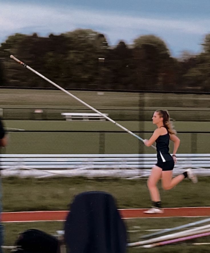 a woman running on a track with a pole in her hand and another person watching