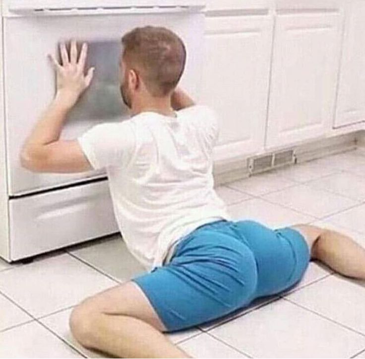 a man sitting on the floor in front of an appliance with his hands up