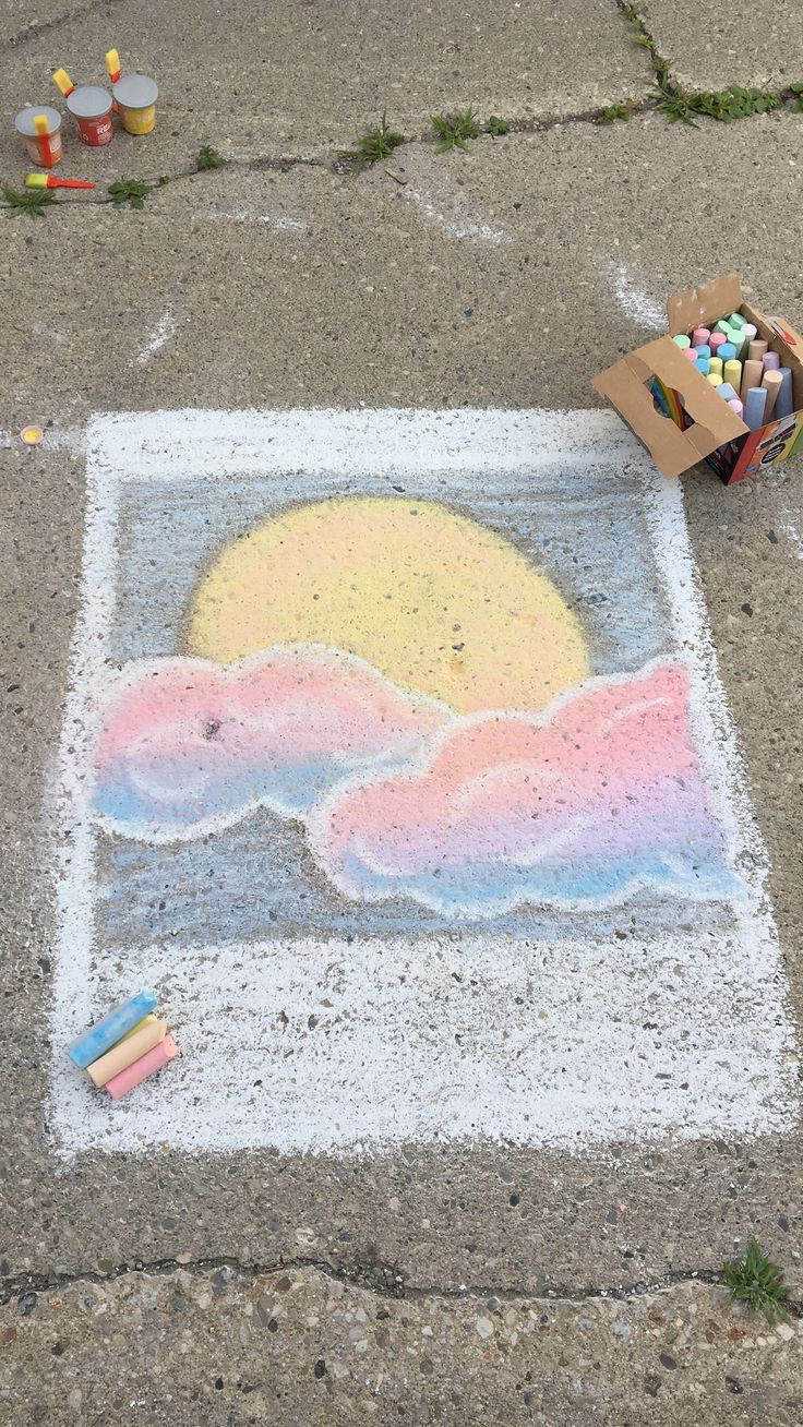 a chalk drawing on the ground with crayons in front of it and a box of crayons next to it