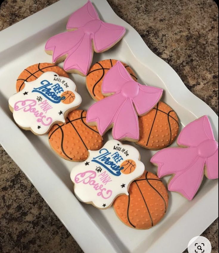 decorated cookies in the shape of basketballs and bows on a white plate with granite counter top