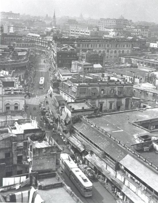 black and white photograph of an old city with lots of buses on the street in front of buildings