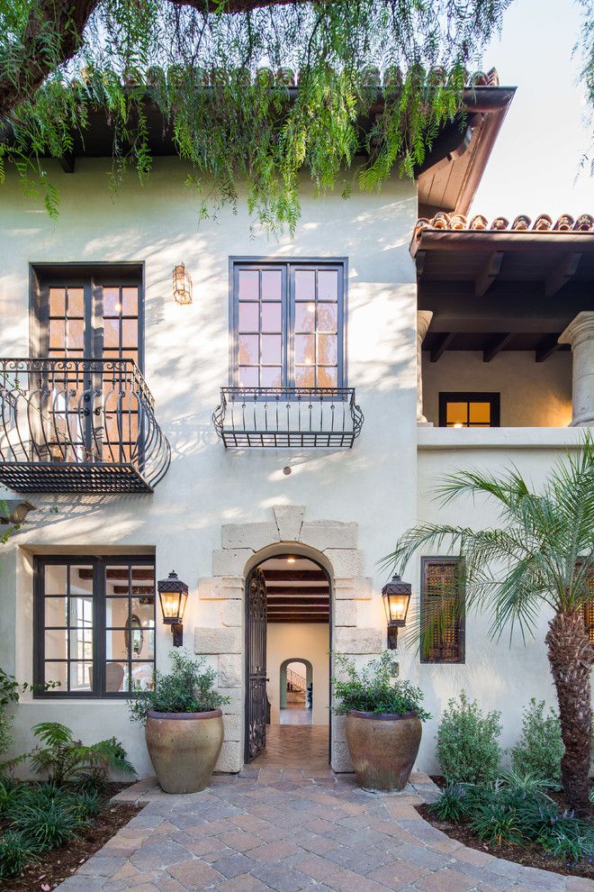 a white house with two balconies and plants on the front door, surrounded by palm trees