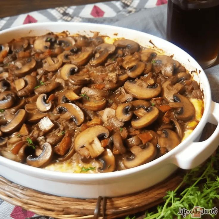 a casserole dish filled with mushrooms on a table next to a glass of beer