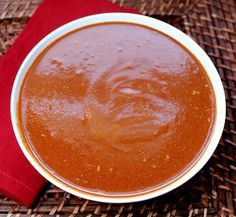 a white bowl filled with red sauce on top of a woven table cloth next to a wooden spoon