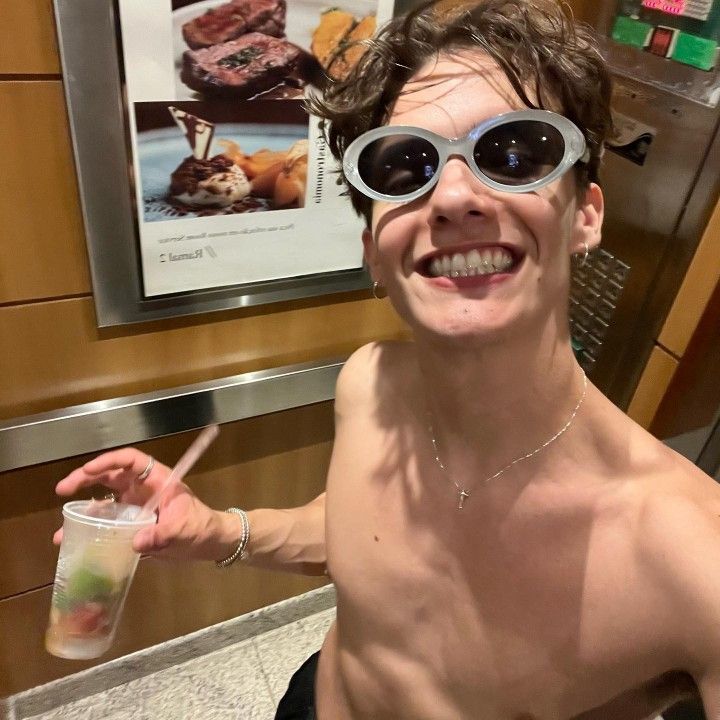 a shirtless man wearing sunglasses and holding a drink