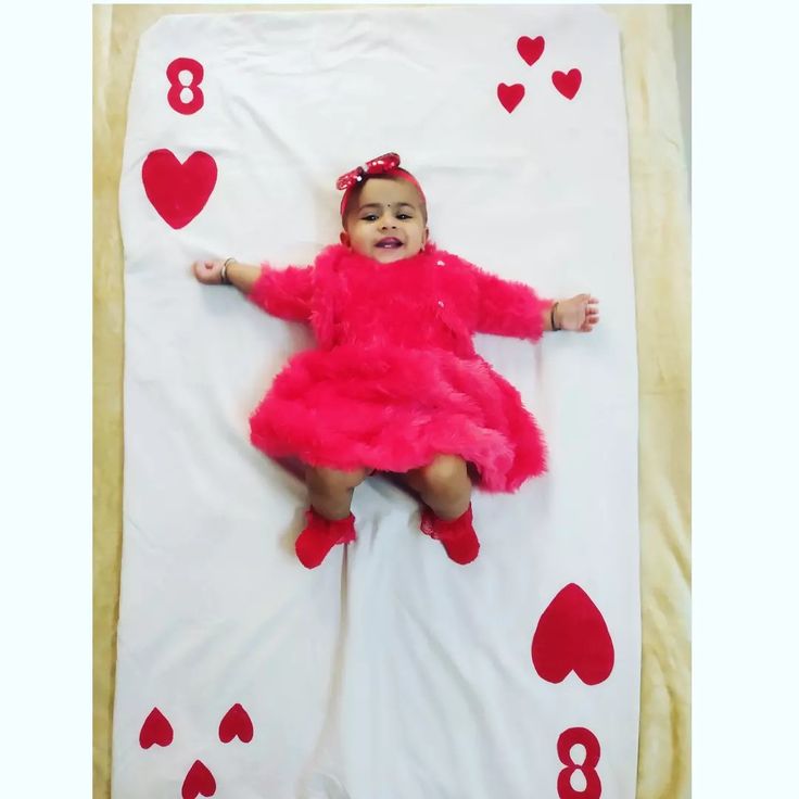 a baby in a pink dress laying on top of a white blanket with red hearts