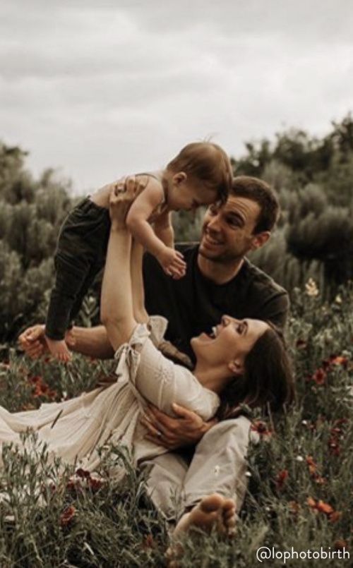 a man, woman and child are laying in the grass with red flowers on them