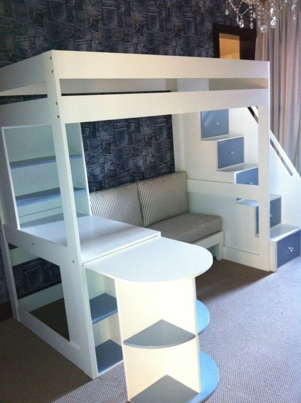 a loft bed with desk underneath and stairs to the upper level, in a room with carpeted flooring