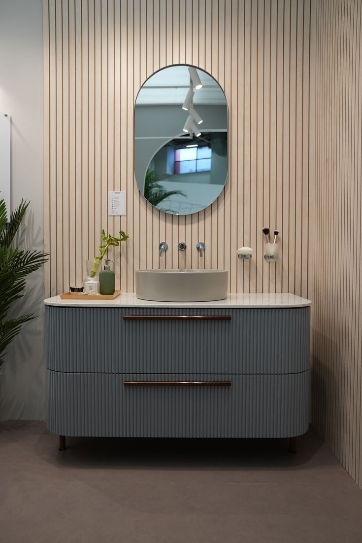 a bathroom with a sink, mirror and plant on the counter top in front of striped wallpaper