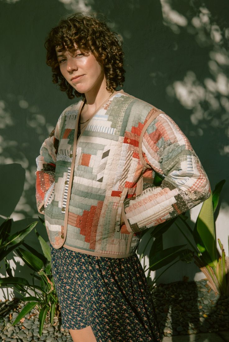 a woman standing in front of a green wall wearing a sweater and floral print skirt