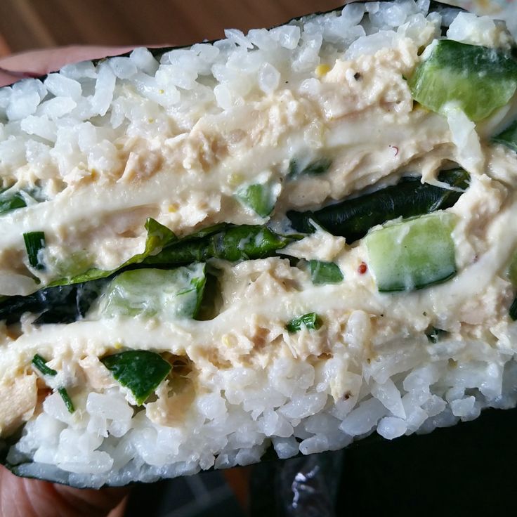 a person holding up a sushi with rice and cucumbers