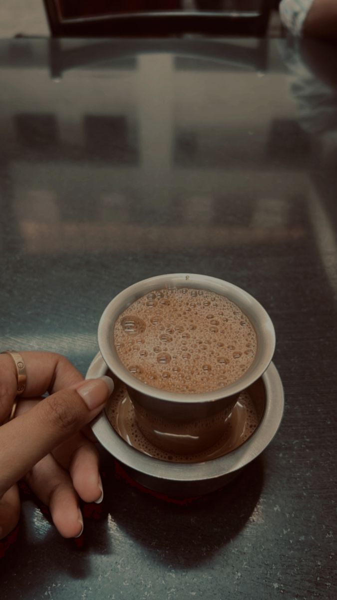 a cup of coffee is being held up by someone's hand on a table