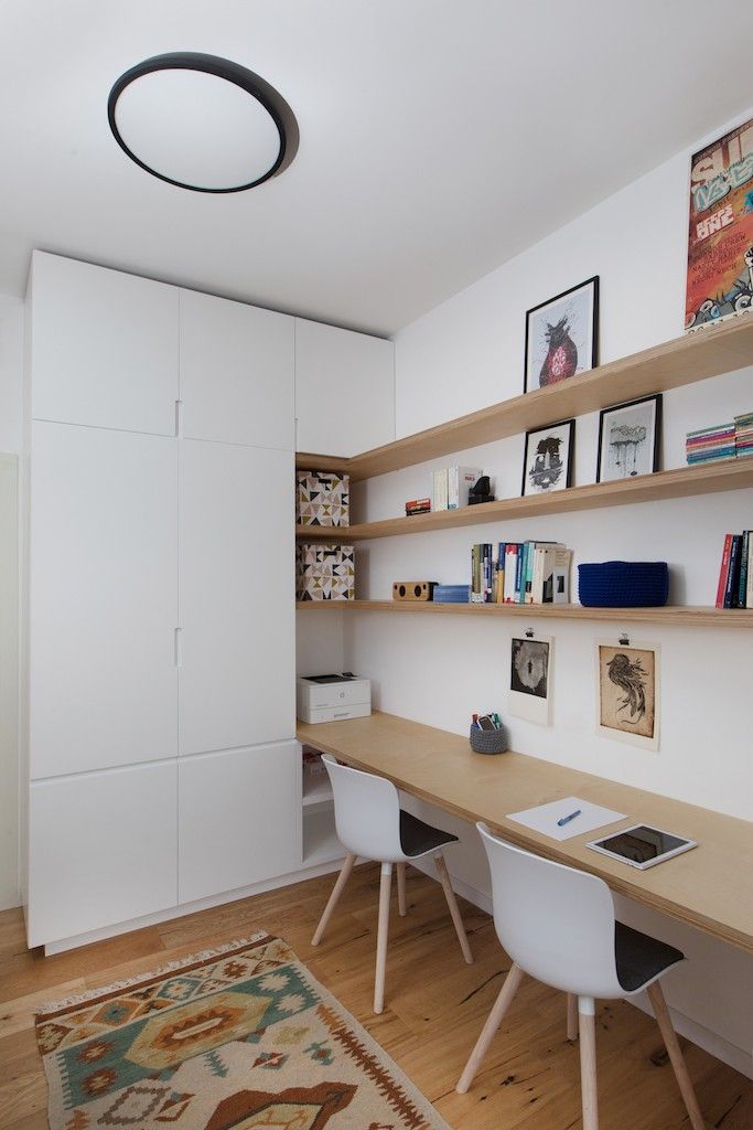 a room with two desks, shelves and pictures on the wall above them in front of a rug