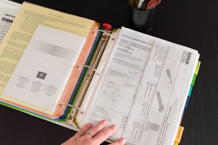 a person's hand is on top of a binder next to an open book