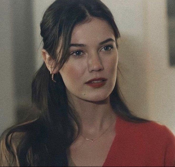 a woman with long hair wearing a red shirt and gold earrings looking at the camera