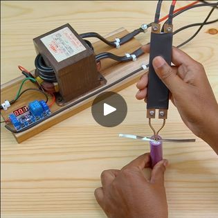 two hands holding scissors and wires connected to an electronic device on a wooden table top