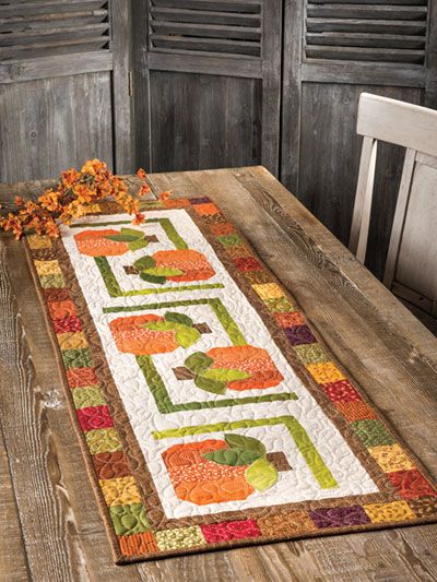 a wooden table topped with an orange and green quilted placemat on top of a wooden table