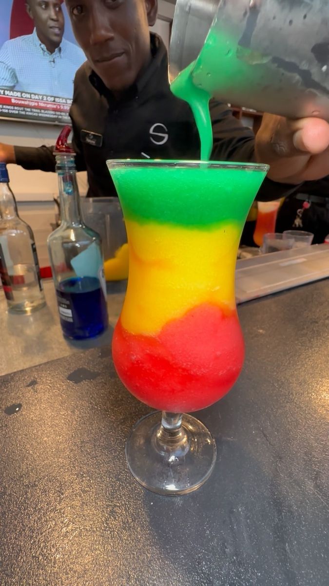 a colorful drink being poured into a glass with a man in the background behind it