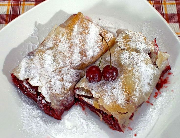 two desserts on a plate with powdered sugar and cherries