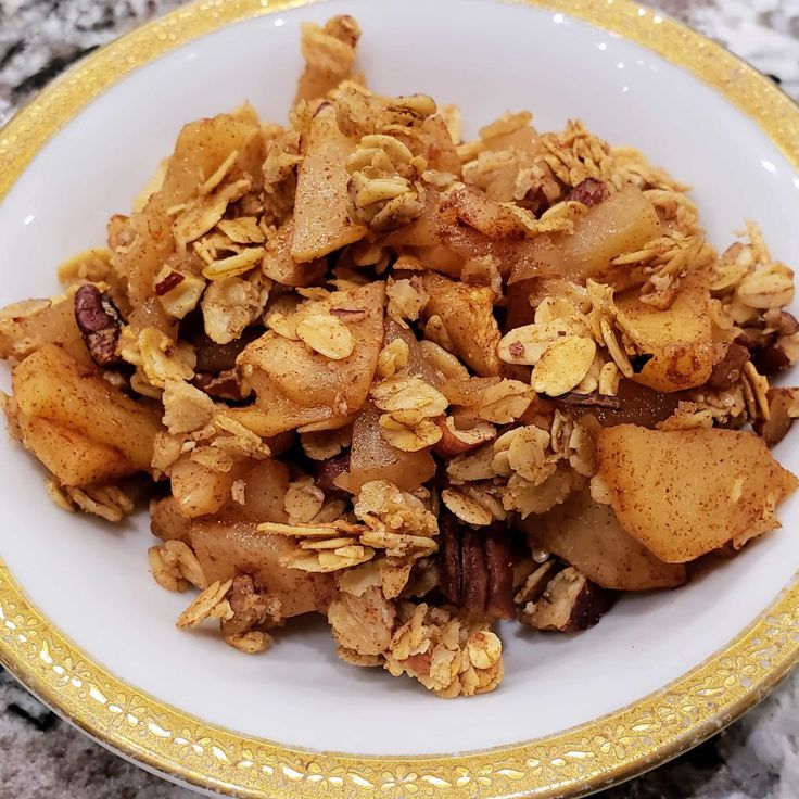 a bowl filled with granola and nuts on top of a marble countertop next to a gold rimmed plate