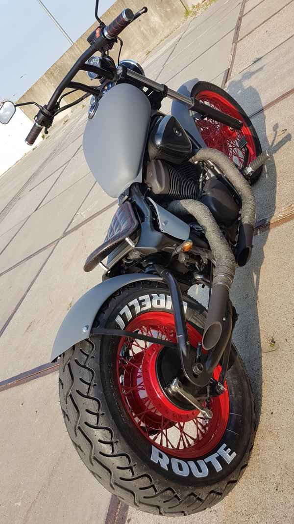 the motorcycle is parked on the sidewalk near the curb with its red tire rims