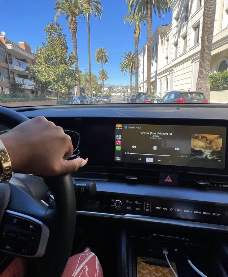 a person driving a car with an electronic screen on the dashboard and palm trees in the background