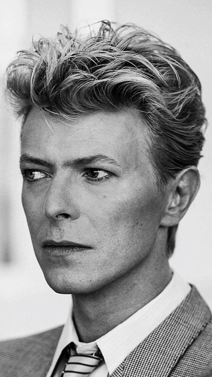 a black and white photo of a man with blonde hair wearing a suit jacket and tie