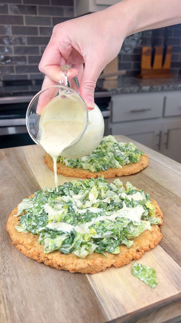 someone pouring dressing on top of two pizzas that are sitting on a cutting board