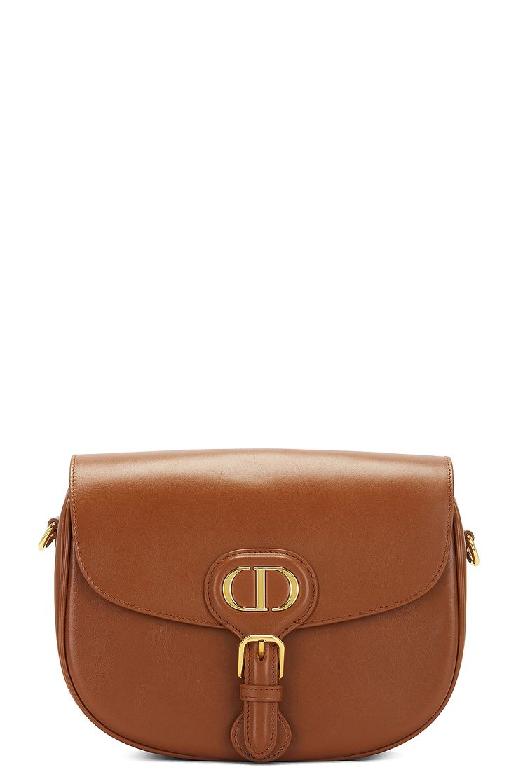 Find DIOR Bobby Bag on Editorialist. The Dior Bobby bag is crafted from leather with suede lining and gold-tone hardware. The bag features a foldover top with a magnetic snap button closure. It includes one main compartment and a single interior flat pocket. The bag comes with original packaging, a dust bag, and a care booklet. It measures approximately 8.7 inches wide, 6.5 inches high, and 2.5 inches deep. The shoulder strap has a 19 inch drop. The bag is in excellent condition with minor creas Chic Bags With Cc Turnlock Closure And Double Flap, Chic Double Flap Bag With Cc Turnlock Closure, Designer Top Handle Flap Bag With Cc Turnlock, Designer Top Handle Flap Bag With Cc Turnlock Closure, Gold Calf Leather Bags With Turn-lock Closure, Luxury Flap Bag With Turn-lock Closure For Daily Use, Luxury Flap Bag For Travel, Luxury Travel Flap Bag, Everyday Luxury Crossbody Shoulder Bag With Turn-lock Closure