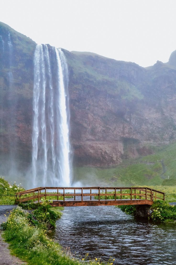 a wooden bridge over a body of water with a waterfall in the background