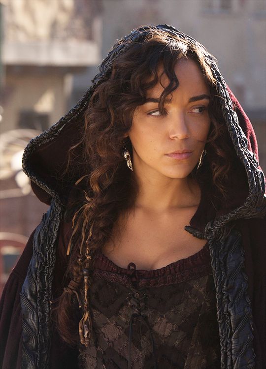 a woman with curly hair wearing a hoodie and looking off into the distance while standing in front of a building