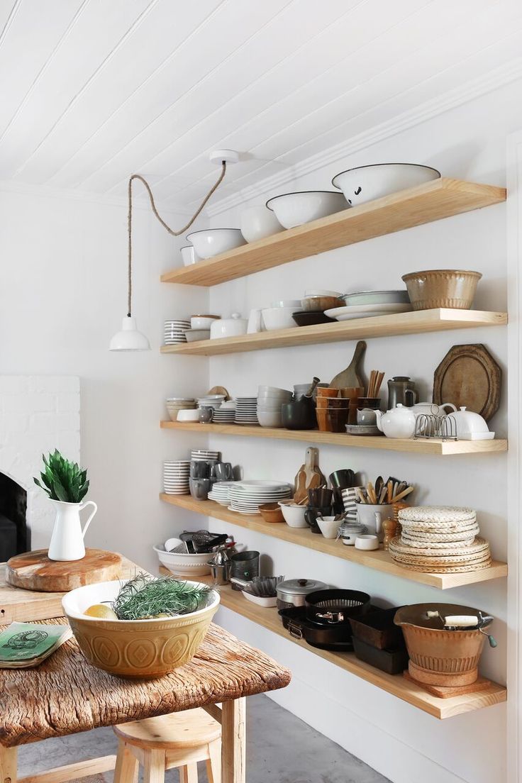 a wooden table topped with plates and bowls next to shelves filled with pots and pans