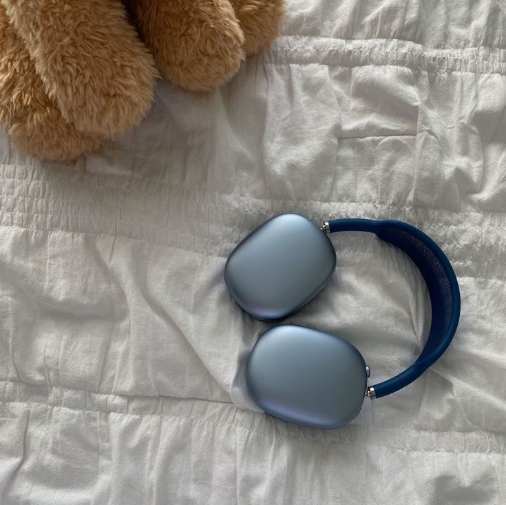 a teddy bear sitting next to two sunglasses on top of a white bed sheet with a blue strap