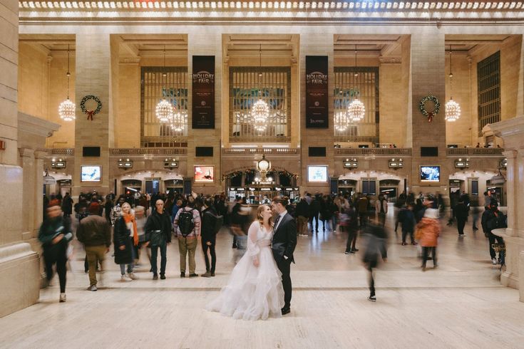 a bride and groom standing in the middle of a busy lobby