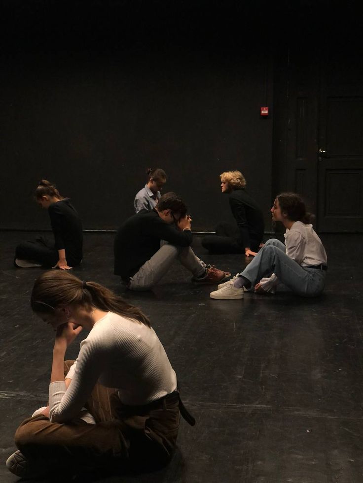 a group of people sitting on the floor in a dark room with one person covering his face