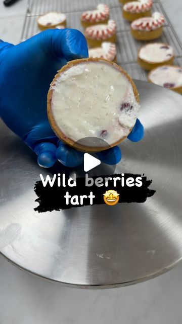 a person in blue gloves holding up a cupcake with white frosting on it