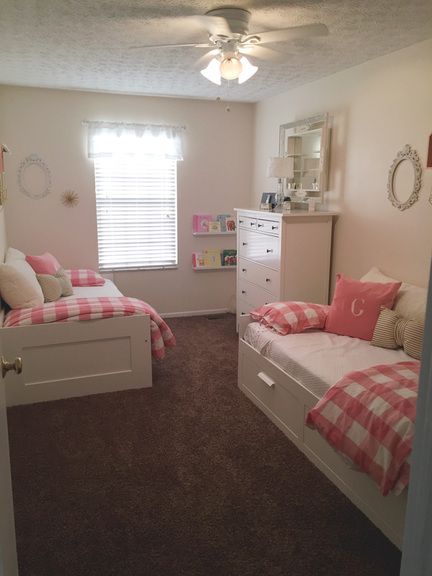 two twin beds in a bedroom with pink and white bedding, dressers and mirror