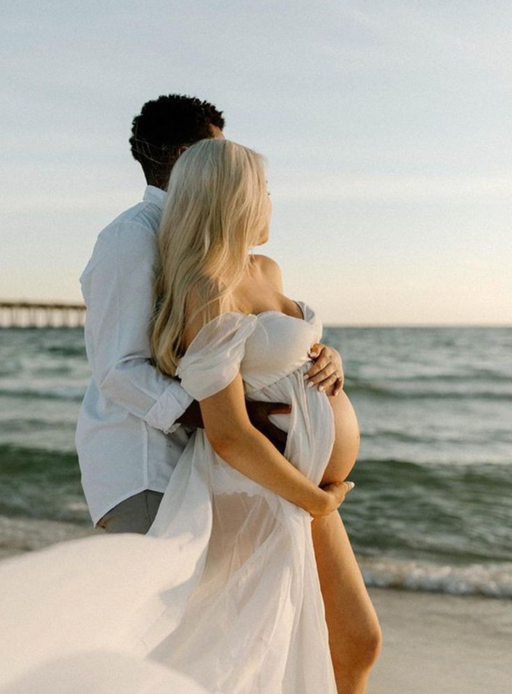 a man and woman are standing on the beach with their arms around each other as they hug