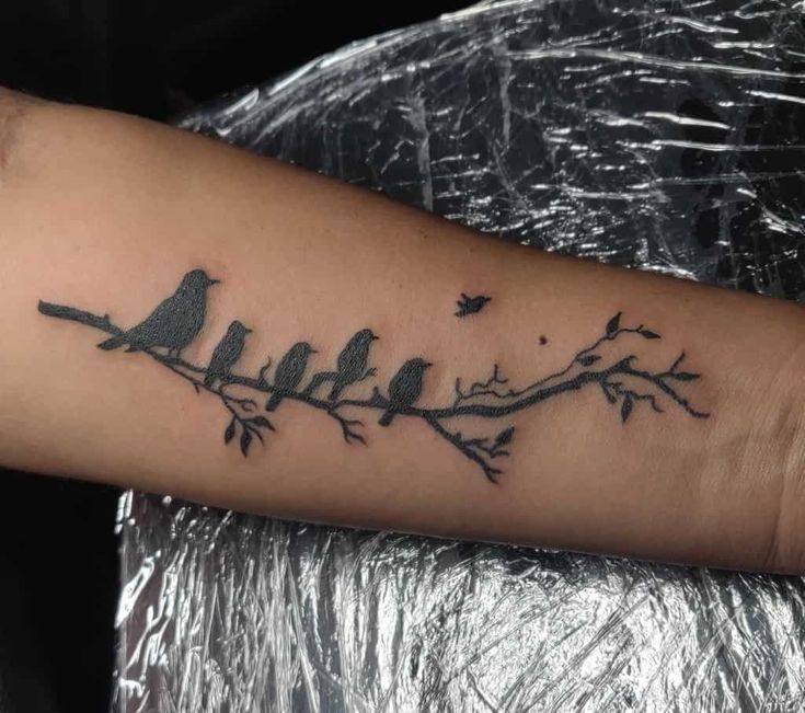 a bird tattoo on the arm with birds sitting on it's branches and leaves