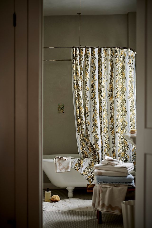 a bath tub sitting under a window next to a shower curtain and towels on the floor