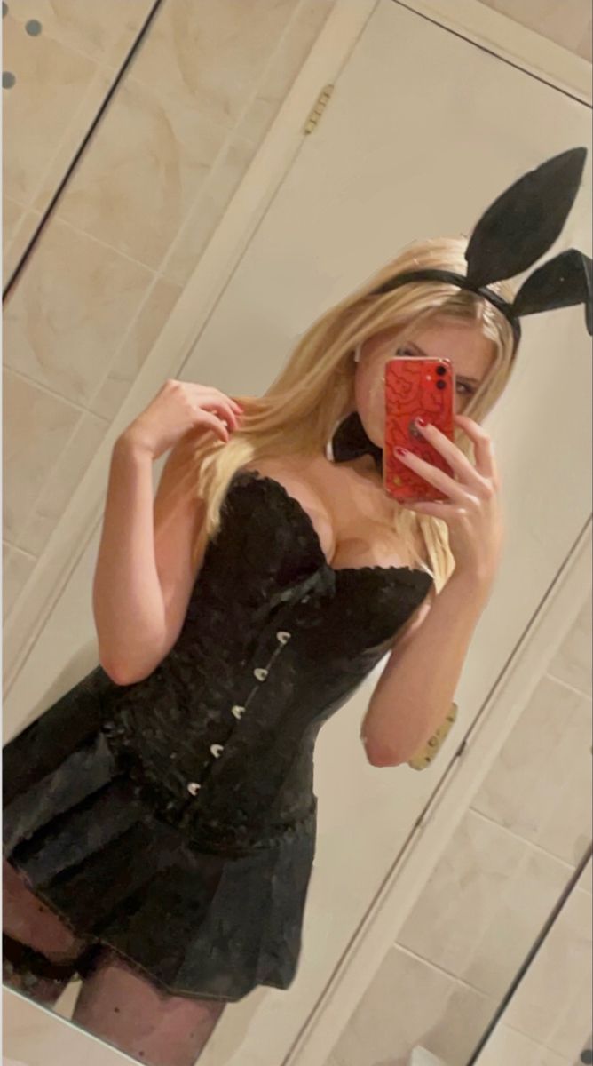 a woman taking a selfie in front of a mirror wearing a black dress and bunny ears