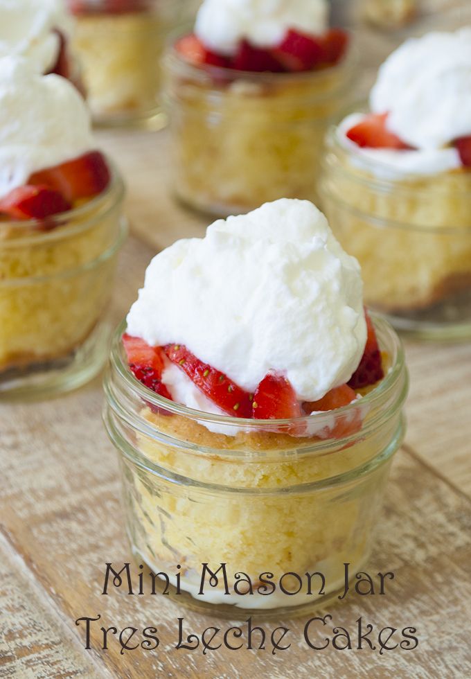 mini mason jar trifle cakes with whipped cream and strawberries in the center on a wooden table